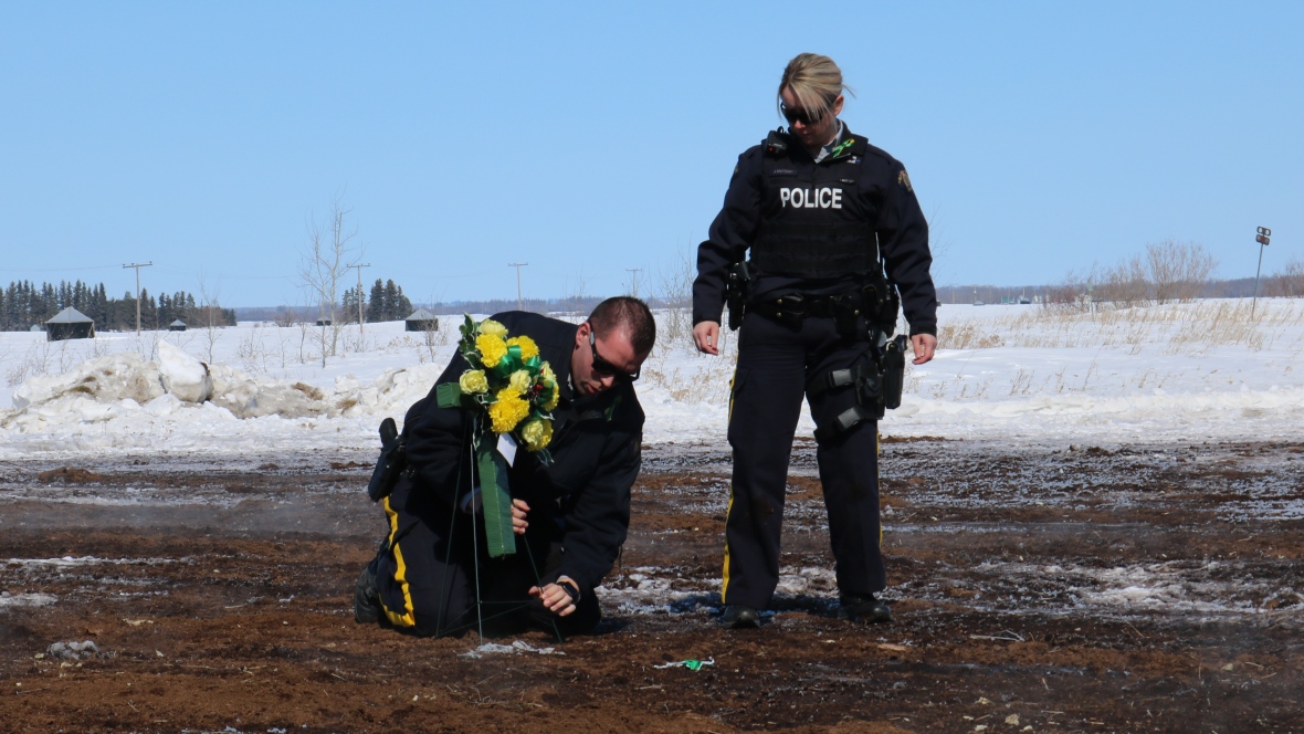 عنصران من شرطة كندا الفدراليّة يضعان باقة من الزهر في موقع الحادثة التي أودت بحياة 15 لاعبا من فريق برونكوس للهوكي/CBC/ هيئة الاذاعة الكنديّة