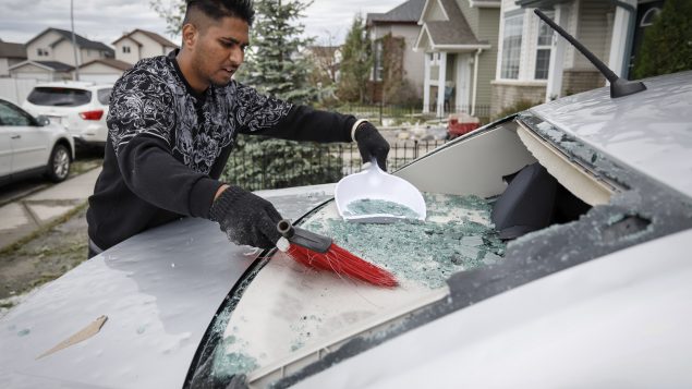 سوك سينغ ينظّف زجاج سيّارته الذي حطذمته حبّات برَد بحجم طابة التنس/Jeff McIntosh/CP