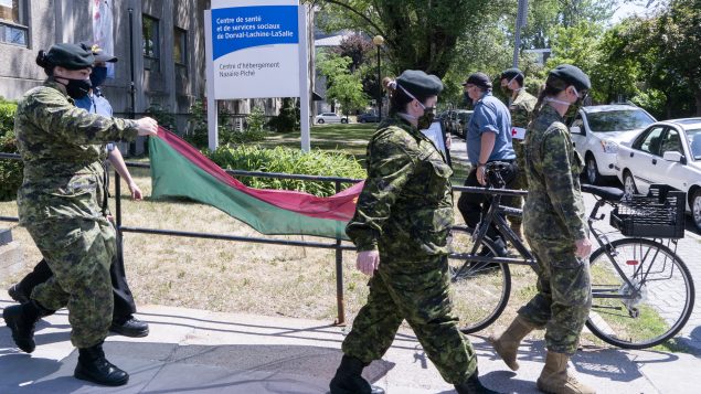 عناصر من الجيش الكندي يحملون علم كتيبتهم لدى مغادرة أحد مراكز رعاية المسنّين في مقاطعة كيبيك/Paul Chiasson/CP