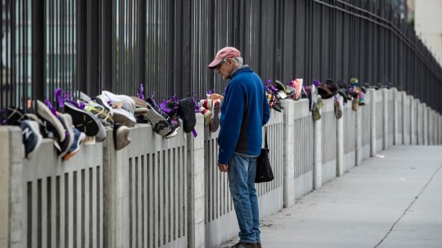 شخص ينظر إلى أحذية ضحايا أشباه الأفيونيّات المعلّقة فوق جسر بورارد في فانكوفر في يوم التوعية على المخدّرات في 31- 07-2020/Darryl Dyck/CP