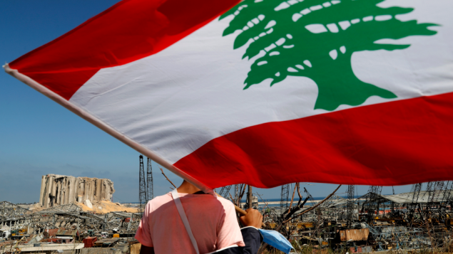 علم لبنان يرفرف على خلفيّة الدمار الذي ألحقه الانفجار في مرفأ بيروت و بعض مناطق العاصمة اللبنانيّة/Ahmad Malla/AP