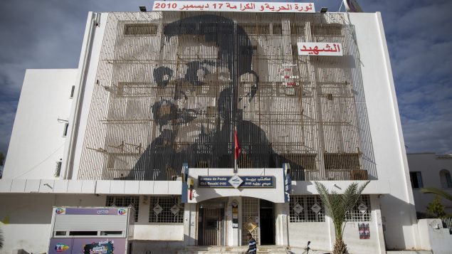 مؤسّسة البريد في مدينة سيدي بوزيد تعلوها صورة محمّد البوعزيزي الذي أضرم النار في نفسه قبل 10 سنوات تجاجا على الفقر وقمع الشرطة له،اقترن اسمه بانطلاق ثورة الياسمين في تونس/Riadh Dridi/AP
