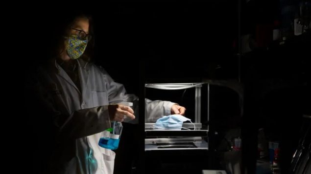 تقوم د. بيليندا هين بتعريض الكمامة للضوء بعد رشّها بمحلول أزرق الميثيلين والماء من أجل تطهيرها من الفيروسات/Riley Brandt/University of Calgary)
