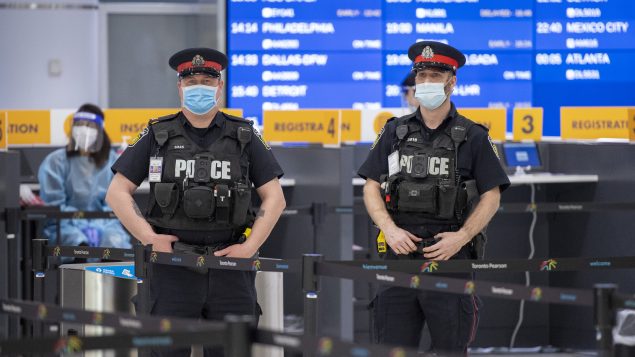 عناصر من الشرطة وعمّال الصحّة في قاعة الوصول في مطار تورونتو حيث يخضع المسافرون الواصلون إلى كندا لاختبار كورونا/Frank Gunn/CP