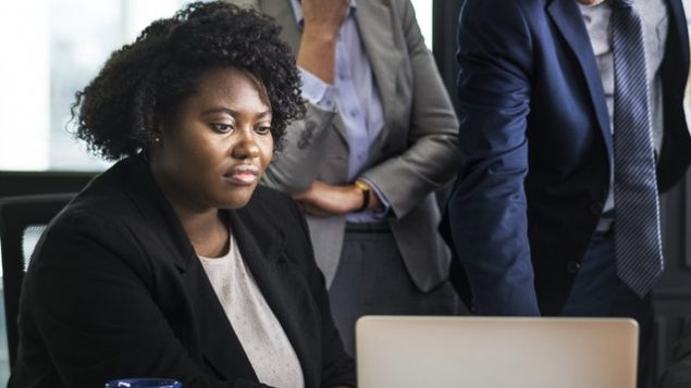 Employee at computer, managers in background.