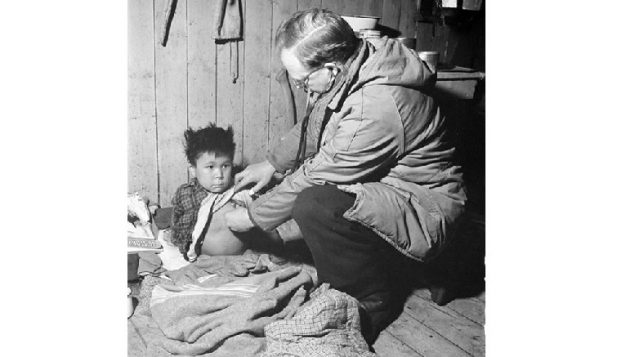 Twice yearly, native settlements were visited by a government doctor. Shown here is T.J.Orford, doctor and agent for the James Bay district, with a child showing signs of tuberculosis. The child will be hospitalized "outside"(ie in southern Canada) at government expense. Jan. 1946 (Library and ARchives Canada, Mikan-3225246)