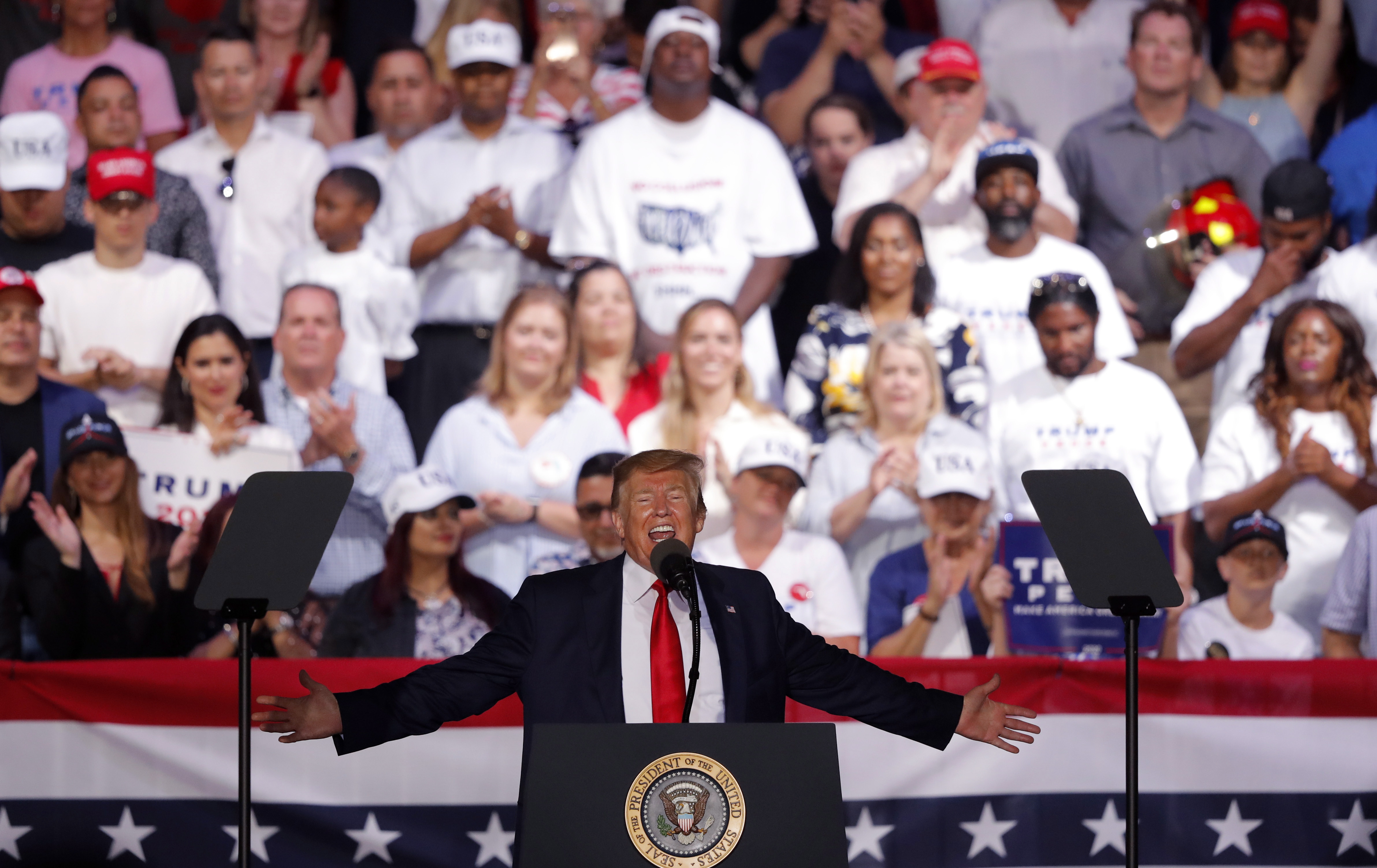 U.S. Pres. Donald Trump with arms outstretched addressing a rally.