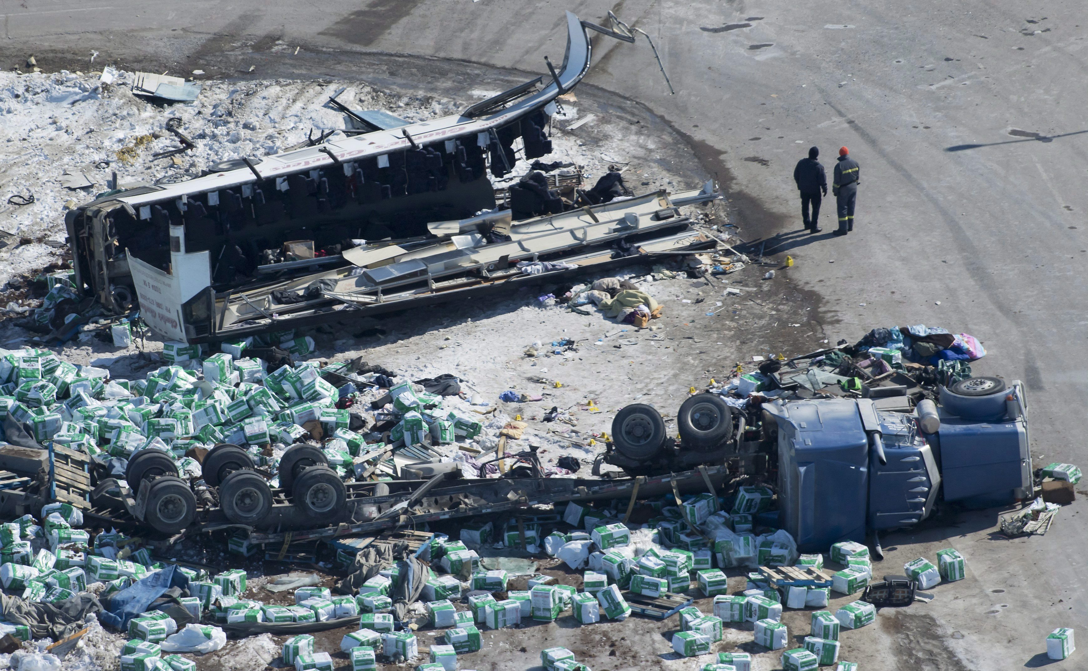 Accident scene involving bus with part sheared off and truck on it side, load scattered.