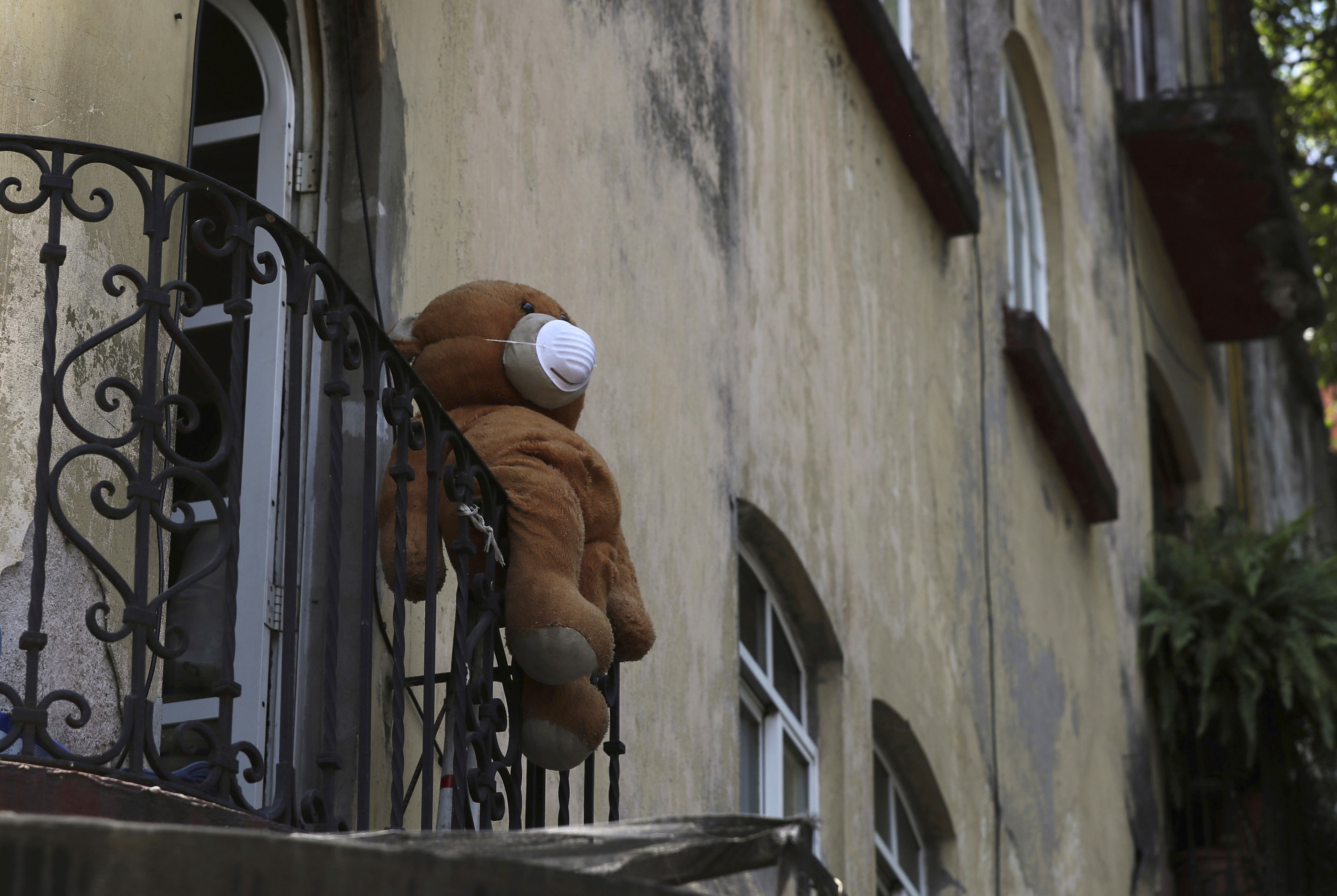 A teddy bear wearing a face mask hangs from a balcony in Mexico City