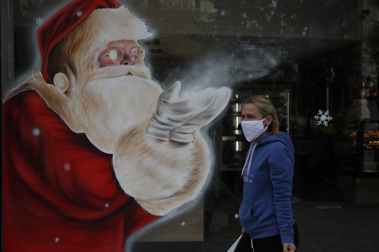 A woman wearing a face mask passes a Santa Claus mural RCI English