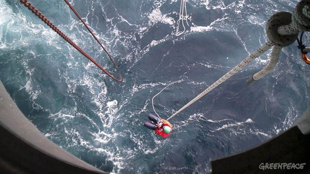 In this Greenpeace photo, an activist scales the underside of Cairn Energy's Leiv Eiriksson oil rig on Sunday. Two activists are suspended under the rig in a survival pod, with about 10 days' worth of food and water. (Greenpeace)