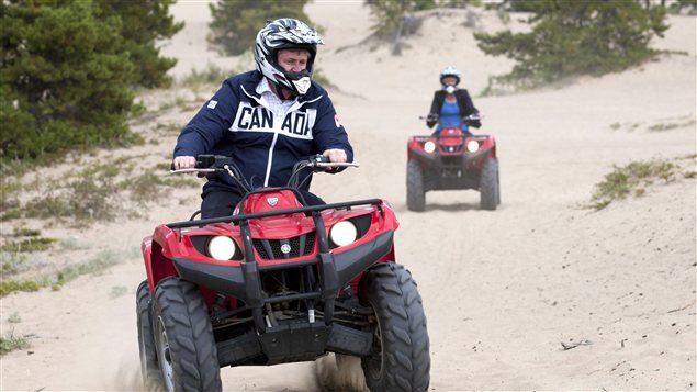 Prime Minister Stephen Harper, front, and his wife Laureen ride an all terrain vehicles around sand dunes near Caribou Crossing, Yukon on Monday. Adrian Wyld/Canadian Press