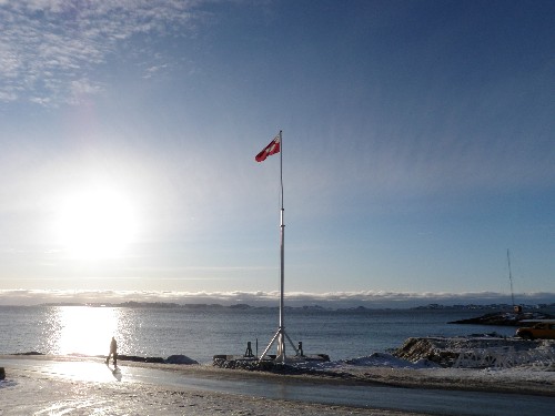 Man walks past Greenlandic flag at sundown.