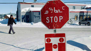 A person walks past a stop sign displayed in both English and Inuktitut in the Nunavut's capital, Iqaluit. (Nathan Denette/Canadian Press)