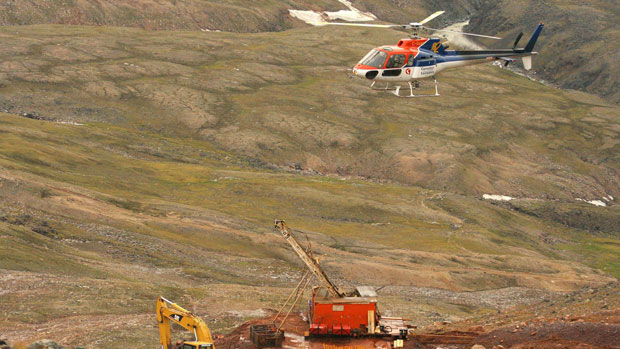 A helicopter passes over excavation equipment at the Mary River exploration camp. Photo: Vinnie Karetak, The Canadian Press