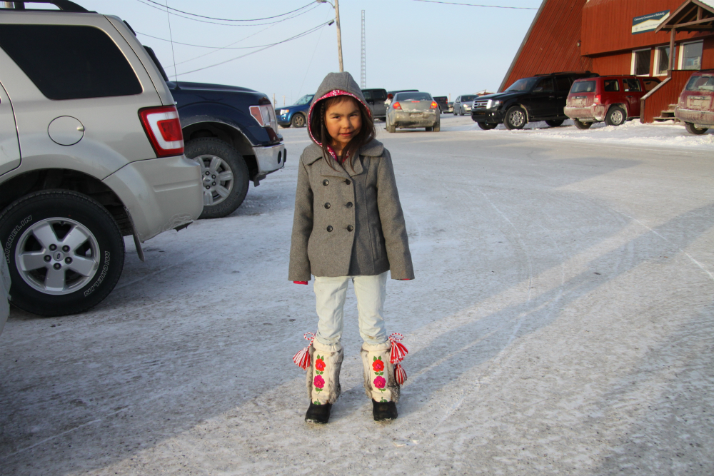 A young girl with intricately embroidered moccasins poses for a photo in the parking lot of the community centre in Behchoko. Photo by Levon Sevunts