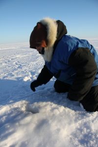 A young Inuit hunter examines a seal breathing hole in the sea ice near Clyde River, Nunavut. Photo by Levon Sevunts.