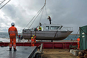 With winds gusting to about 75 km/h during a sudden snowsquall, Canadian Coast Guard crew members manoeuvre Parks Canada's vessel the Investigator and its support cradle over to the well deck of the Sir Wilfrid Laurier for transportation to the survey area as a support vessel for the search of the Franklin ships. (Parks Canada)
