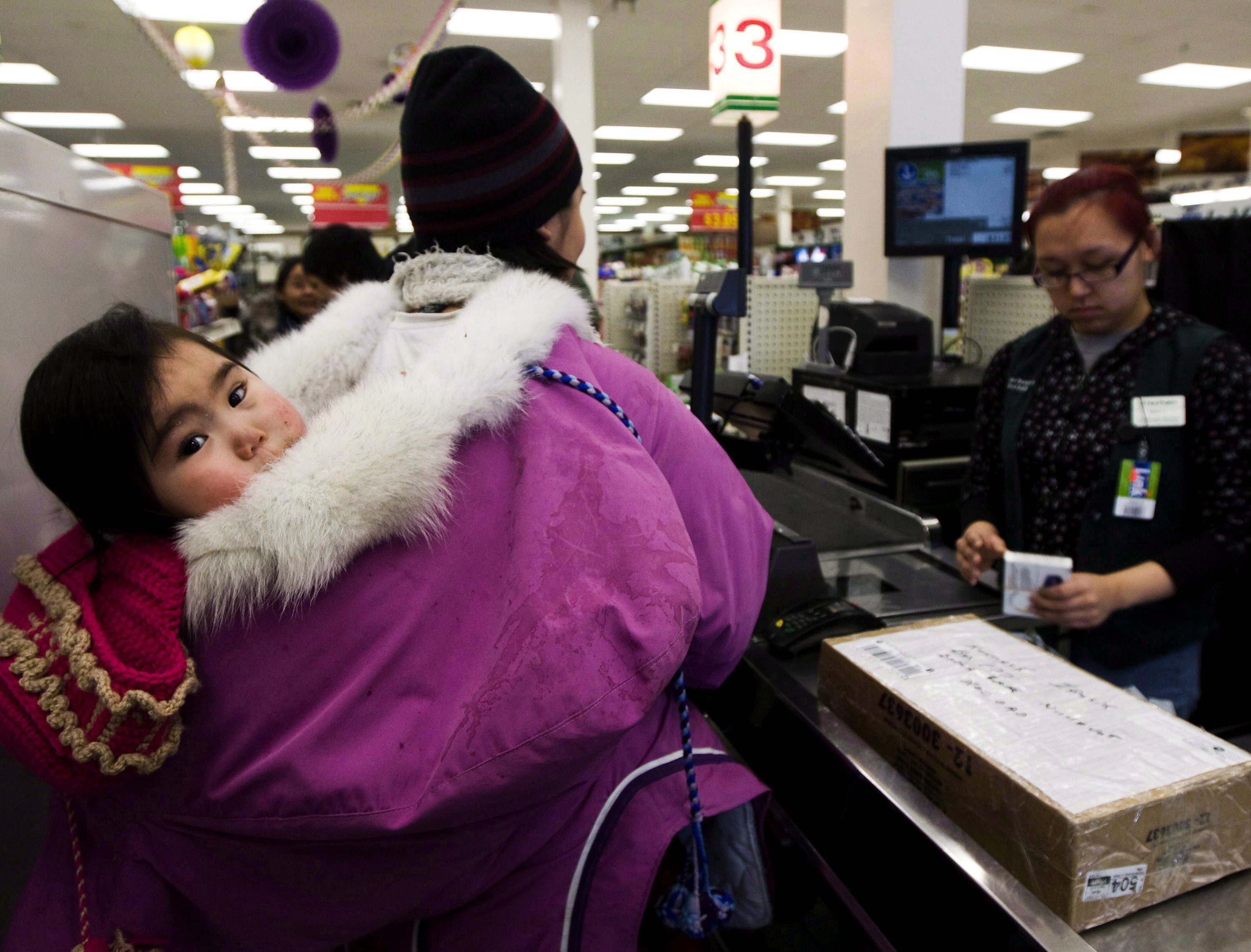 Food security is an issue in communities across the North. Here, Pauline Kadjuk, 1, is carried in a Amautik by her mother Brittany Ikulik, middle, while paying for groceries at the Northern store in the small town of Baker Lake, Nunavut. (Nathan Denette / The Canadian Press)