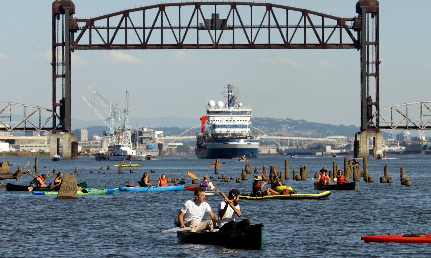 oaters gather as the Royal Dutch Shell PLC icebreaker Fennica heads under a railroad bridge and up the Willamette River in Portland, Ore., Thursday, July 30, 2015. The Fennica left dry dock and made its way down the Willamette River toward the Pacific Ocean soon after authorities forced the demonstrators from the river and the St. Johns Bridge. (Don Ryan/AP)