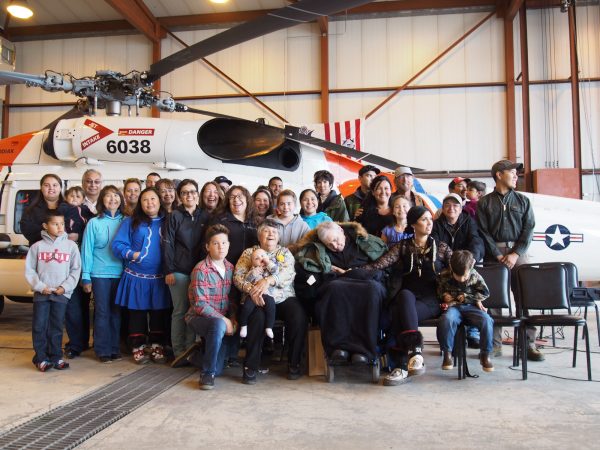 Members of the Schaeffer family pose for a picture after the dedication ceremony. Mary Schaeffer sits in the front row, next to John, pictured wearing a green jacket. (Zachariah Hughes/ Alaska Public Media – Kotzebue)