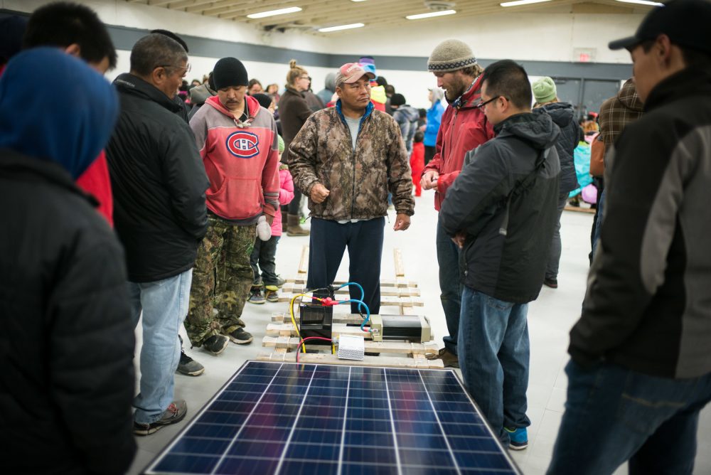 Lootle Arreak (in red) and Esa Quillaq (in camouflage) speak with Vancouver Renewable Energy Coop Solar Installer, Duncan Martin about solar panels, at Clyde River community centre. (Greenpeace)