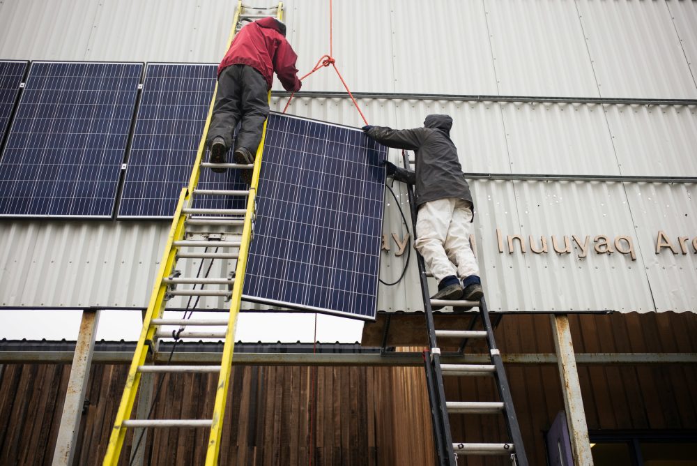 Vancouver Renewable Energy Coop Solar Installer, Duncan Martin (L) and Logistics Coordinator for Greenpeace Canada, Claude Beausjour install solar panels at the Clyde River community centre. Greenpeace came to deliver solar panels and offer a series of lectures and workshops in Clyde River. (Greenpeace)