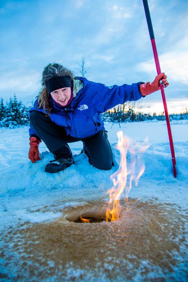 Research associate professor Katey Walter Anthony inspects flaming methane gas seeping from a hole in the ice on the surface of a pond on the UAF campus. The naturally occurring phenomenon is made worse by thawing permafrost and increased plant decay caused by global warming. (Todd Paris / UAF)