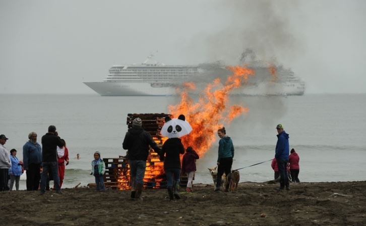 A bonfire blazes on the beach as the Crystal Serenity cruise ship lies at anchor in Nome on Sunday, Aug. 21, 2016. The bonfire was part of a polar swim in the Bering Sea. Locals swam in the cold water as a few ship passengers watched from shore. (Bob Hallinen / Alaska Dispatch News)