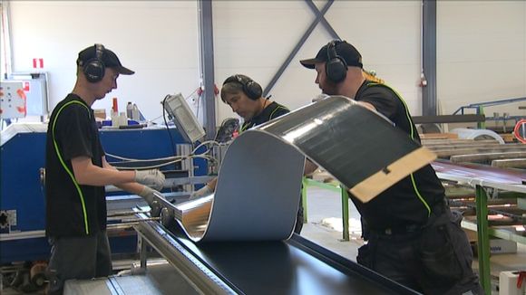 Workers attach photovoltaic film to roofing material. (Samuli Holopainen / Yle)
