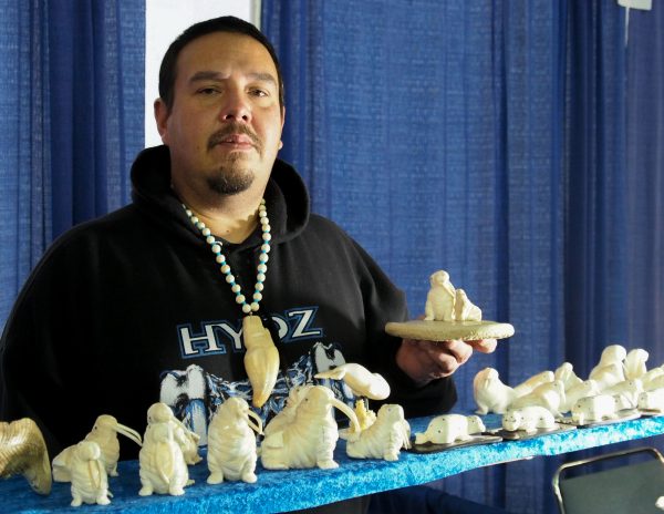 Dennis Pungowiyi shows off one of his favorite carving motifs, a mother walrus with her pup. (Zachariah Hughes/Alaska Public Media)