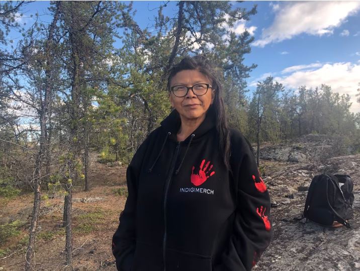 Tłı̨chǫ teacher and homelessness activist Georgina Franki stands in the forest.
