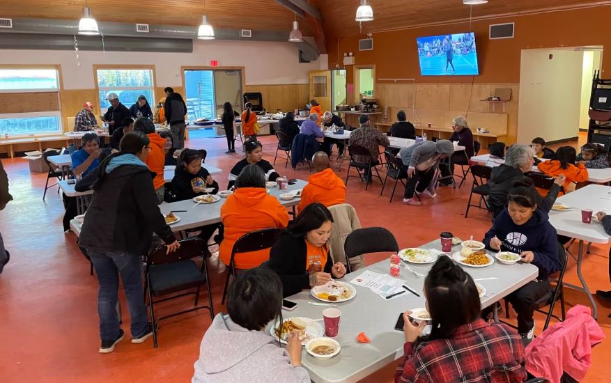 Community members eat together, many wearing orange shirts