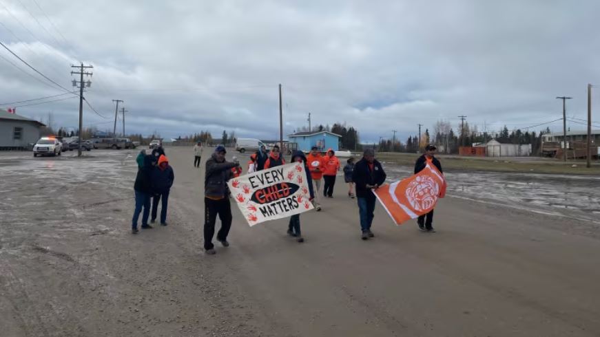 People walking wearing orange shirts and carrying handpainted signs saying every child matters