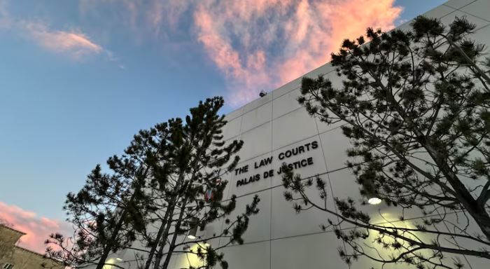 An off-white building with a sign reading "THE LAW COURTS." Two trees are in front of the building. A blue sky with vibrant clouds is above.