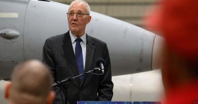 A man speaking at a podium inside an aircraft hangar.