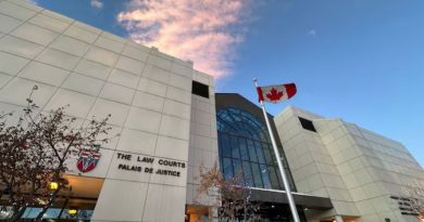 An off-white building with a large multi-story glass window. A sign on the building says "THE LAW COURTS." And Canadian flag is out front.