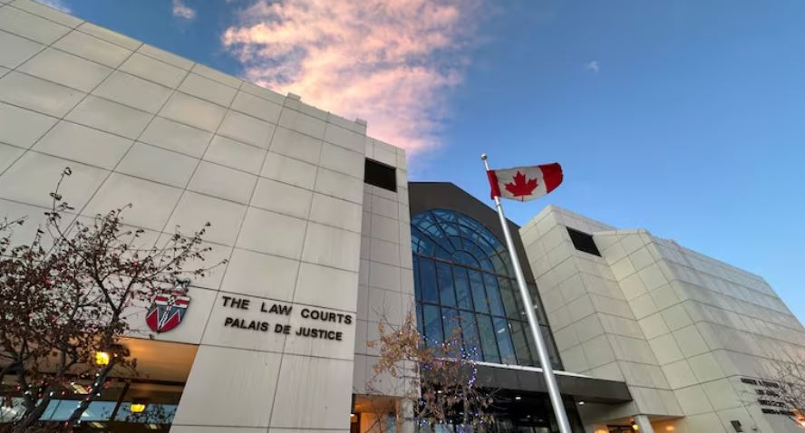 An off-white building with a large multi-story glass window. A sign on the building says "THE LAW COURTS." And Canadian flag is out front.