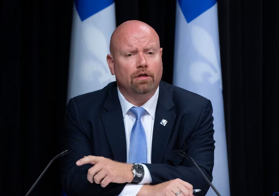 Ian Lafrenière speaking at a conference flanked by Quebec flags.