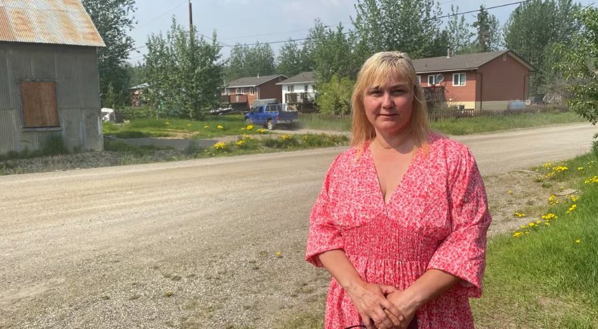 A woman stands by a dirt road in a town.