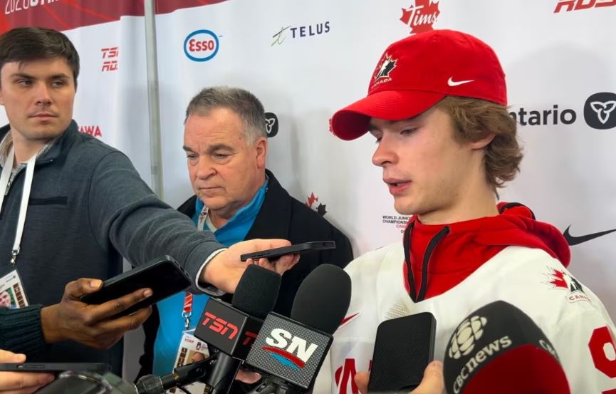 A young hockey player in a media scrum. There are two other men to his left.