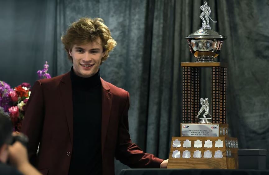 A young man in a sport coat poses with a trophy.