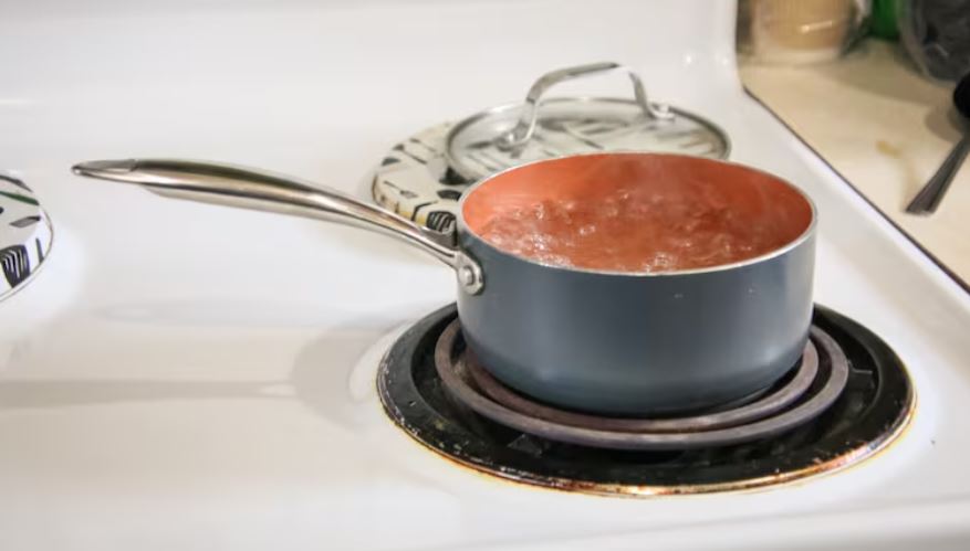 A pot of water is seen boiling on a stove element
