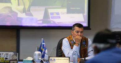 Tłı̨chǫ Grand Chief Jackson Lafferty sits at a table with a projector screen behind him in Whatì in mid-July 2022.