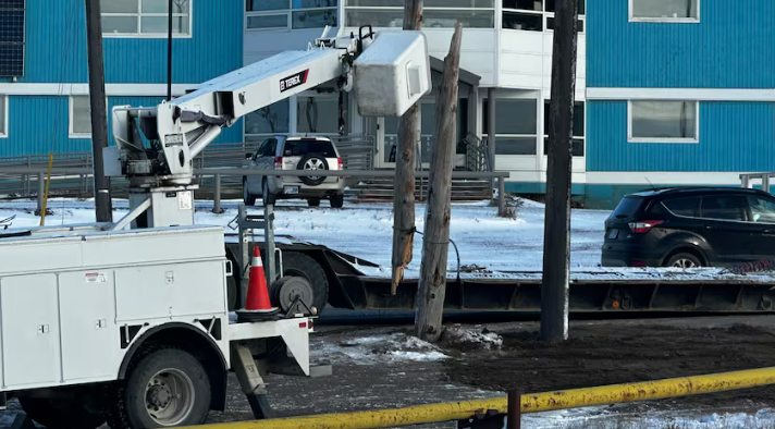 A machine near a broken power pole in front of a blue building.