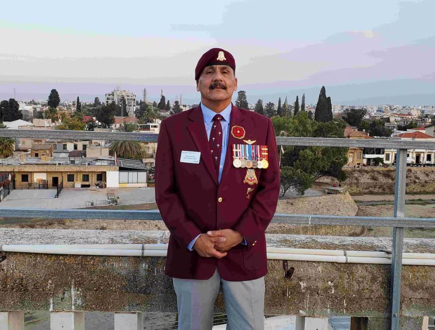 A man stands in a military jacket and smiles at the camera 