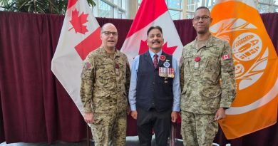 Three men stand together, with two of the men wearing army uniforms