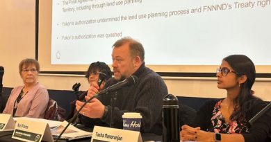 A man speaks into a microphone at a table with others.