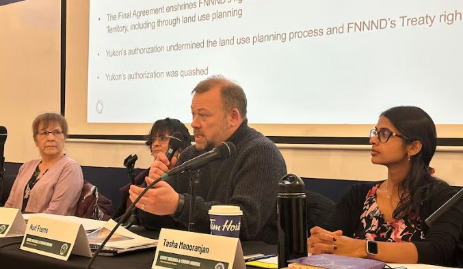 A man speaks into a microphone at a table with others.