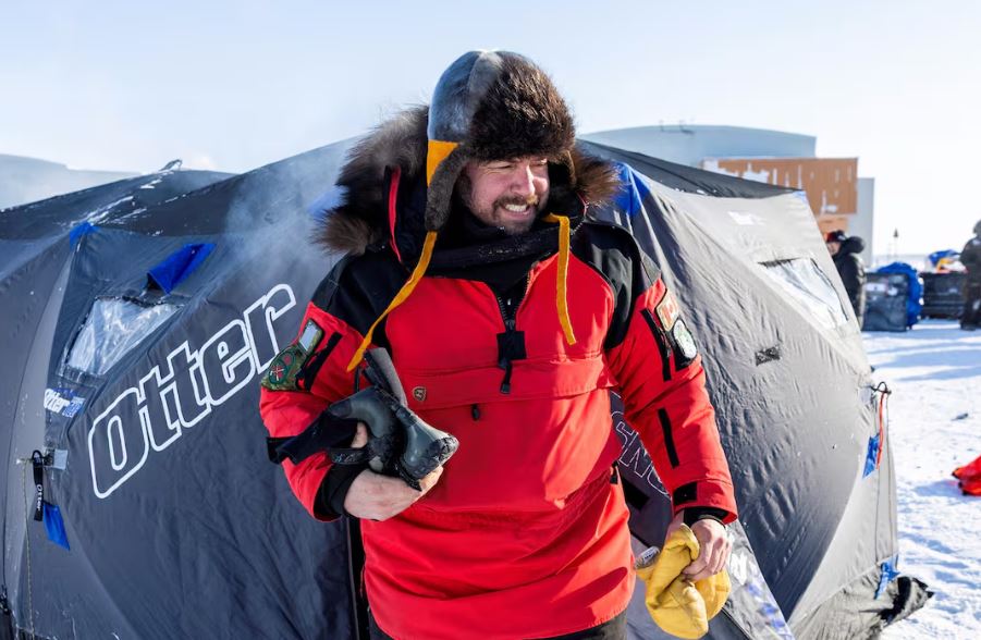 A man in red parka and trapper hat exiting a tent.